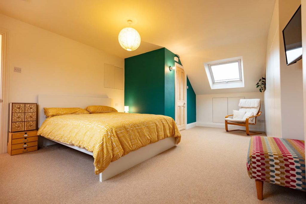Double bedroom with a green feature wall, rooflight and armchair in a Horfield dormer loft conversion