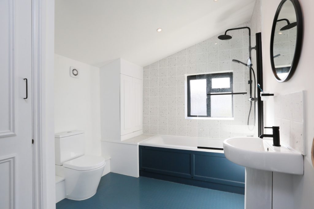 Refitted first-floor bathroom with speckled tiles and a blue bath panel in an Easton house refurbishment, Bristol
