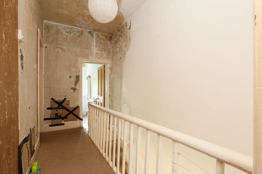 Landing and stairwell before refurbishment, with stripped plaster, in Easton, Bristol