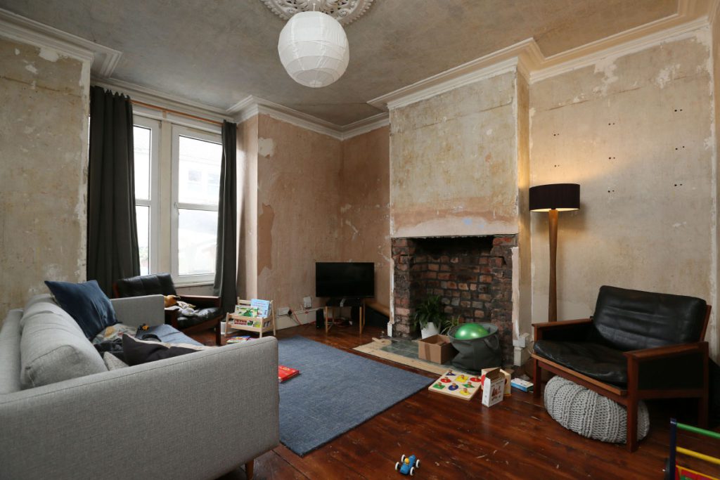 Front living room before refurbishment, with stripped walls and an exposed brick fireplace, in Easton, Bristol