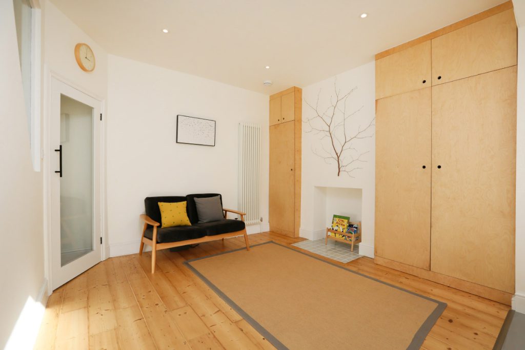 Living room with bespoke plywood storage and a glass-panelled door to the stairwell in an Easton refurbishment, Bristol