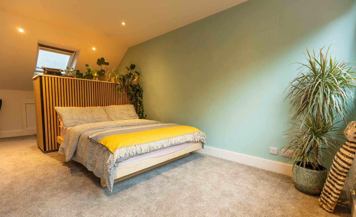 Loft bedroom with sage-green walls and a slatted timber headboard in a full-width dormer conversion in Bedminster, Bristol