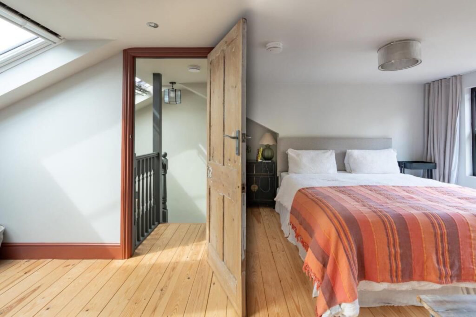 Loft bedroom with natural wood floors and a reclaimed pine door to the staircase in a Montpellier full-width dormer conversion, Bristol