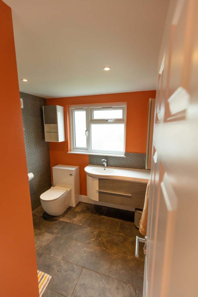 Landing-accessed loft bathroom with orange walls, slate-tiled floor and vanity basin in a Brislington hip-to-gable conversion
