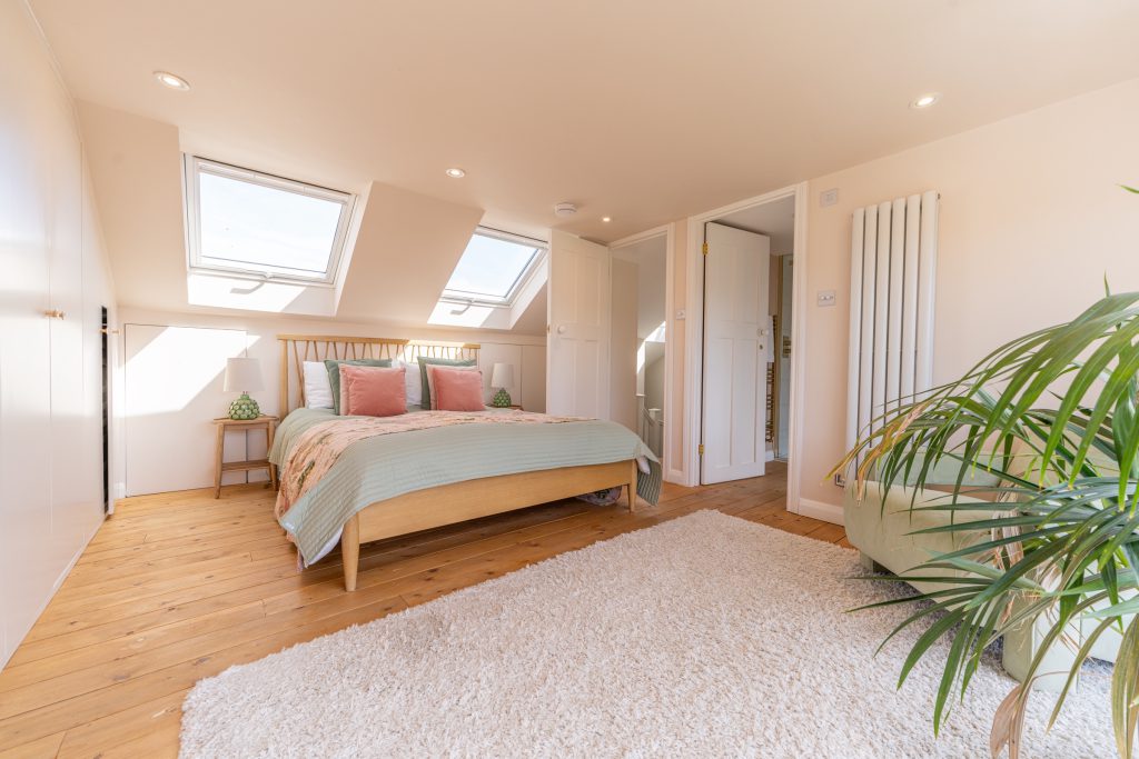 Loft bedroom with twin skylights and a natural wood floor in a low-ceiling dormer conversion in Horfield, Bristol
