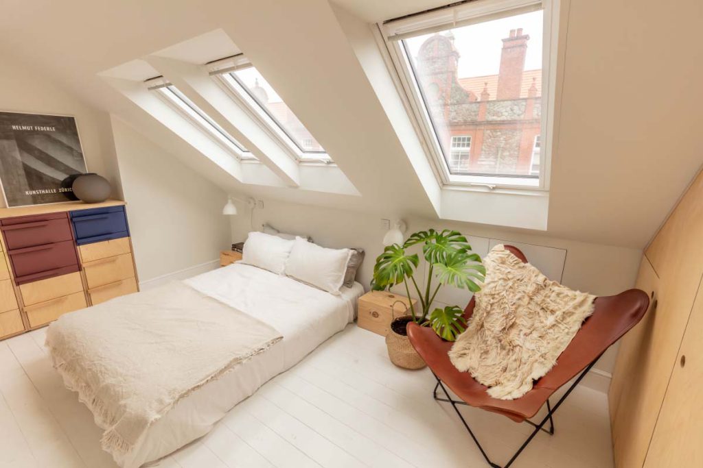 Airy loft bedroom with a leather butterfly chair below roof windows in a Montpellier skylight conversion