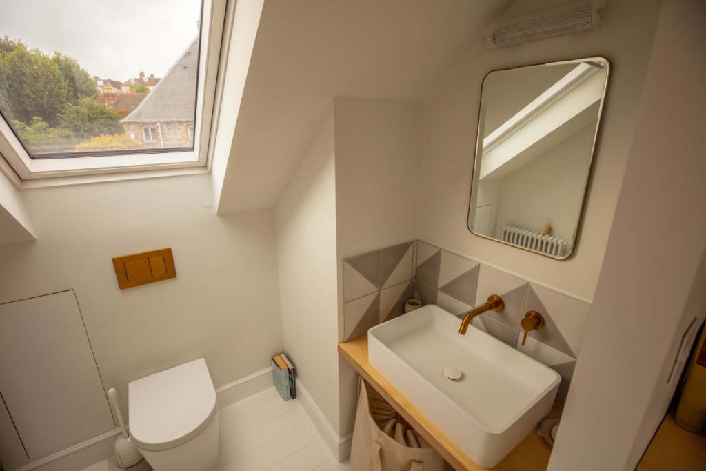 En-suite basin on a bespoke ply vanity with brass tap below a skylight in a Montpellier loft conversion