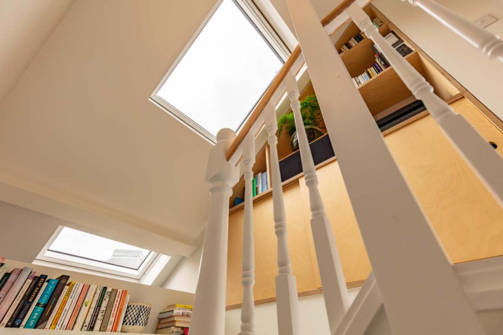 View up to twin skylights and bespoke ply shelving beside the white staircase in a Montpellier loft conversion